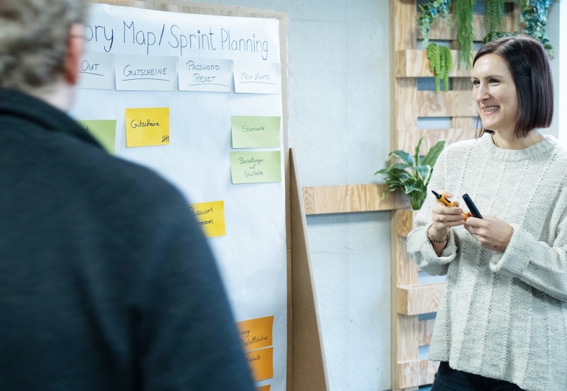 A woman standing next to a pin board,  holding a pen in her hand. On the pin board it reads 