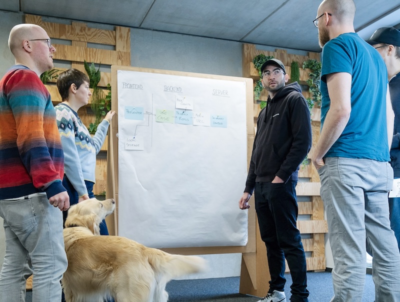 Five people discussing a topic in front of a pin board with sticky notes